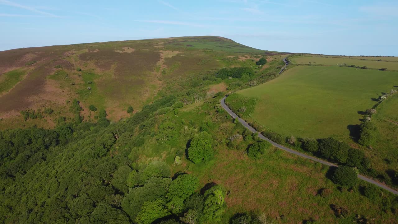 English Countryside with Sprawling Moor and Winding Country Road in Early Morning with Trees and Farmland Fields with Clear Blue Sky Above.