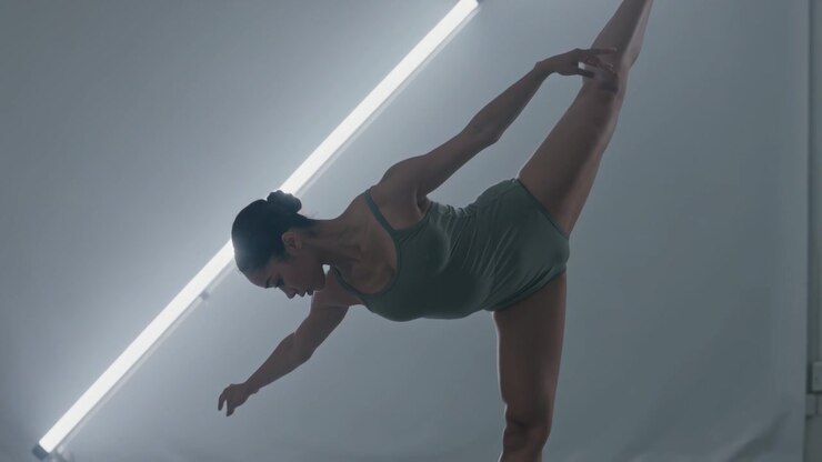 Ballerina in equilibrio con body verde che tiene la gamba sollevata sulle punte in studio con luce, scarpette da punta.