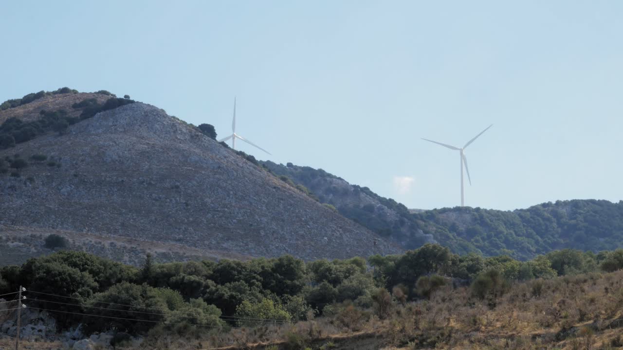 vista lejana de las turbinas eólicas que generan energía alternativa detrás de las colinas en la isla agia kiriaki en grecia