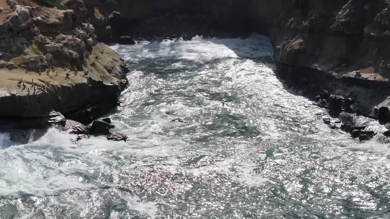 Sol skinner på bølger, der slår mod klipper i en bugt på en strand i La Jolla, Californien, med en tilbagetrækkende luftoptagelse.
