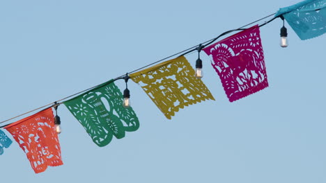 colorful papel picados and string lights hang against a bright blue sky, creating a festive and vibrant scene, perfect for celebrating cultural events or outdoor gatherings.
