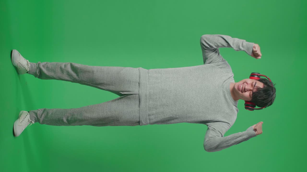 Full Body Of Asian Man Listening To Music With Headphones And Dancing In The Green Screen Studio