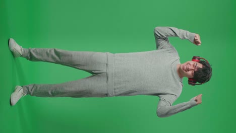 cuerpo lleno de hombre asiático escuchando música con auriculares y bailando en el estudio de pantalla verde