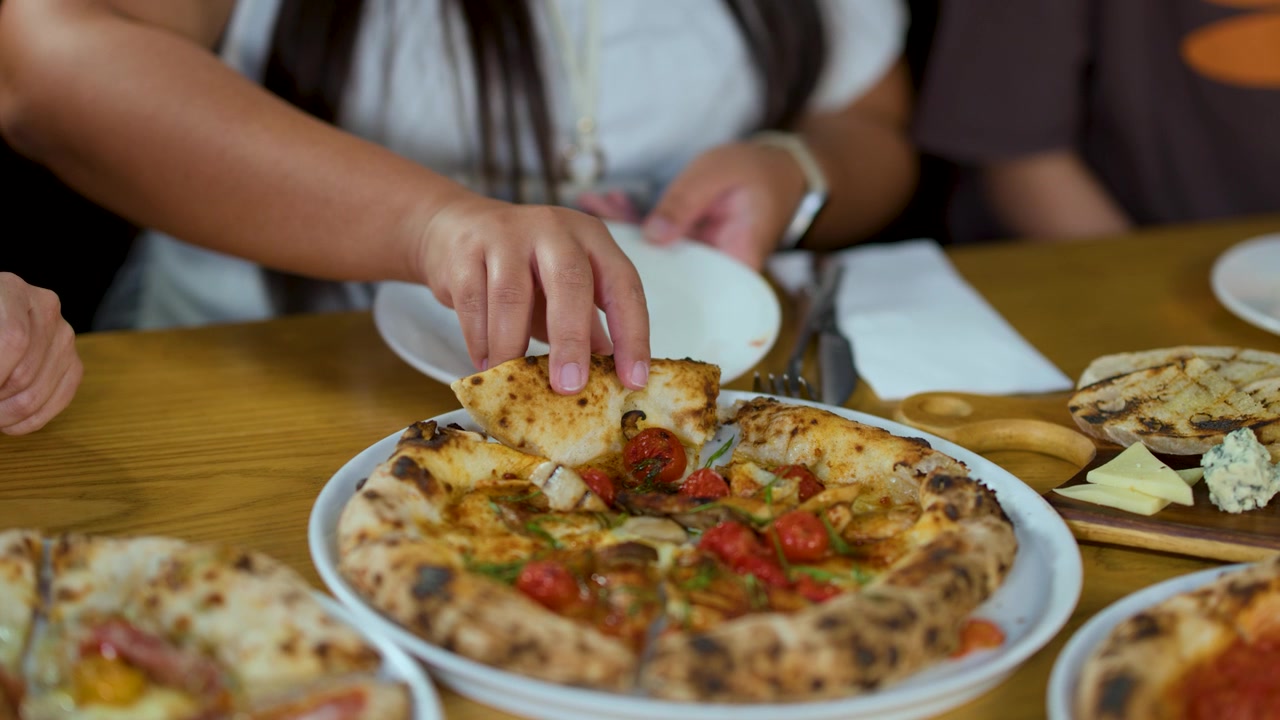 Primo piano di una persona che prende una fetta di pizza durante una cena di gruppo