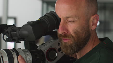 close up of male film camera operator looking through eyepiece shooting movie or video in studio 1