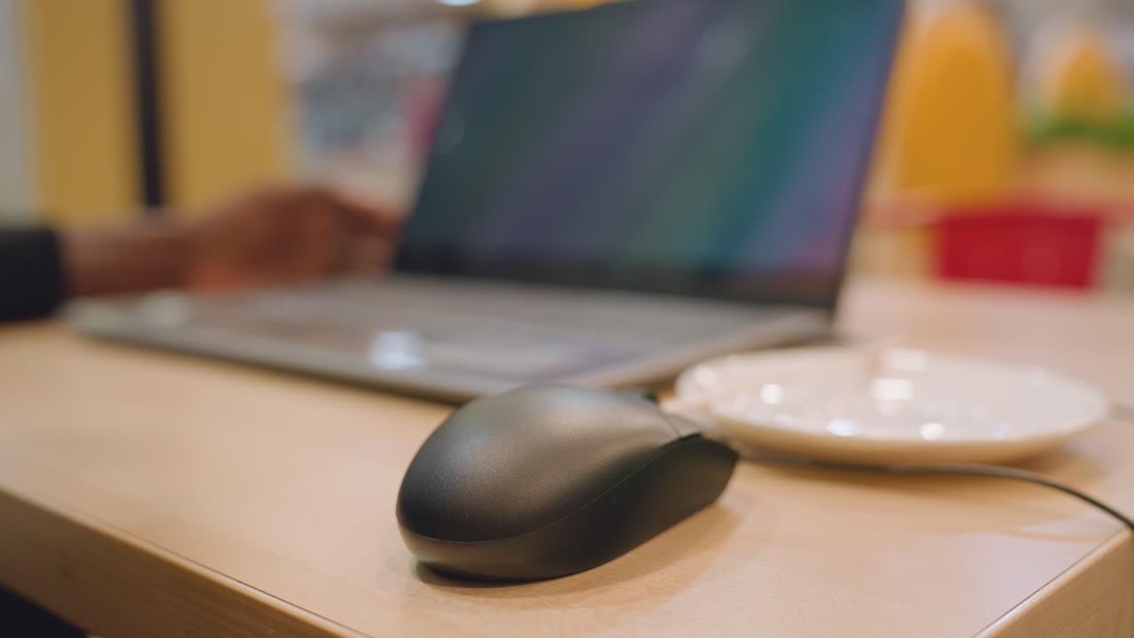 Individual editing presentation while sitting casually. Closeup of person using mouse with laptop nearby. Casual workspace scene with individual editing and multitasking on digital devices