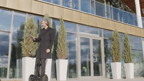 businessman on self-balancing scooter using tablet outside modern office building