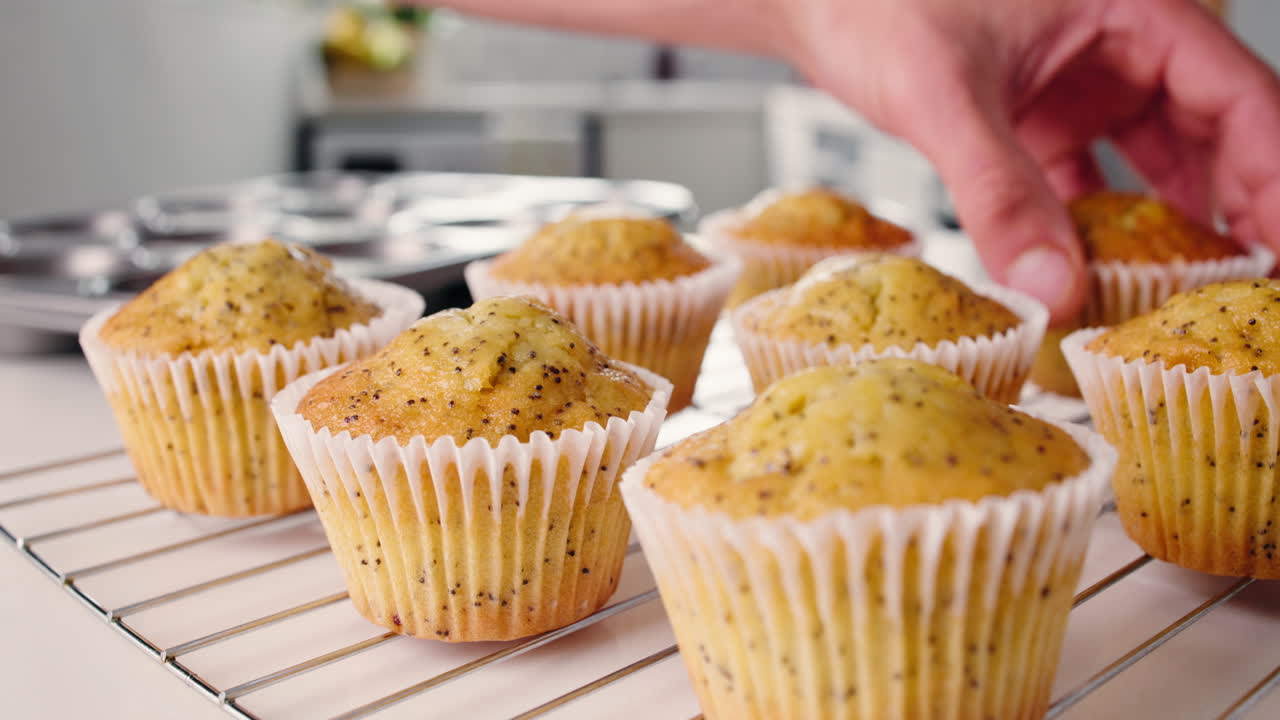 Mano che appoggia muffin ai semi di papavero appena sfornati su una griglia di raffreddamento