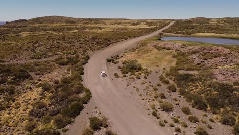 white colored car is passing on the endless road leading through natural landscape during sunshine day, aerial recorded in the mountains of patagonia, argentina, south america