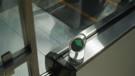 a close-up shot capturing the movement of black boots on an escalator going down. the focus is on the escalator steps and the green directional light