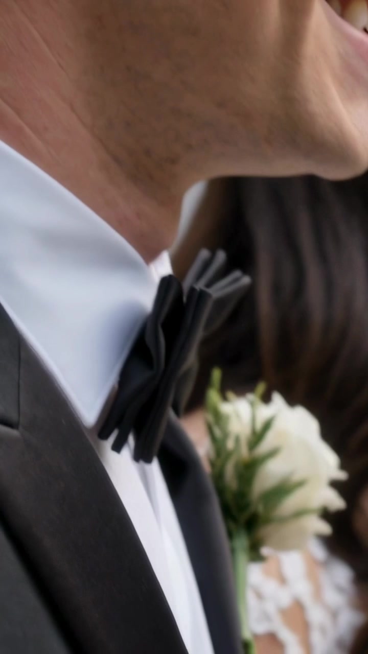Video verticale: Mentre i petali cadono, lo sposo sorride, si inclina al matrimonio, mostrando papillon, spilla e abito di pizzo.