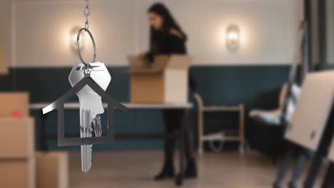 Animation-of-hanging-golden-house-keys-against-blurred-view-of-woman-unpacking-boxes