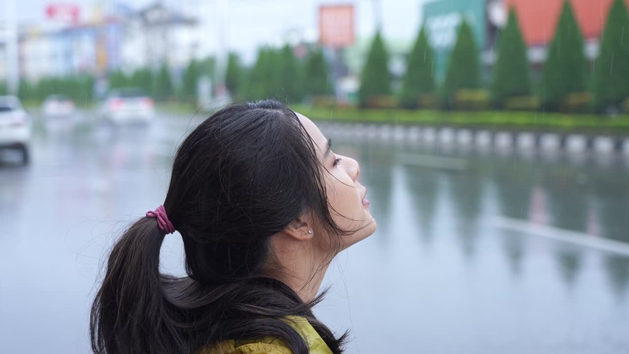 Beautiful carefree asain woman stands on city roadside looking up to sky check for raining, season changes or global warming concept, walking outside in rain, waterproof make up, getting fresh in rain