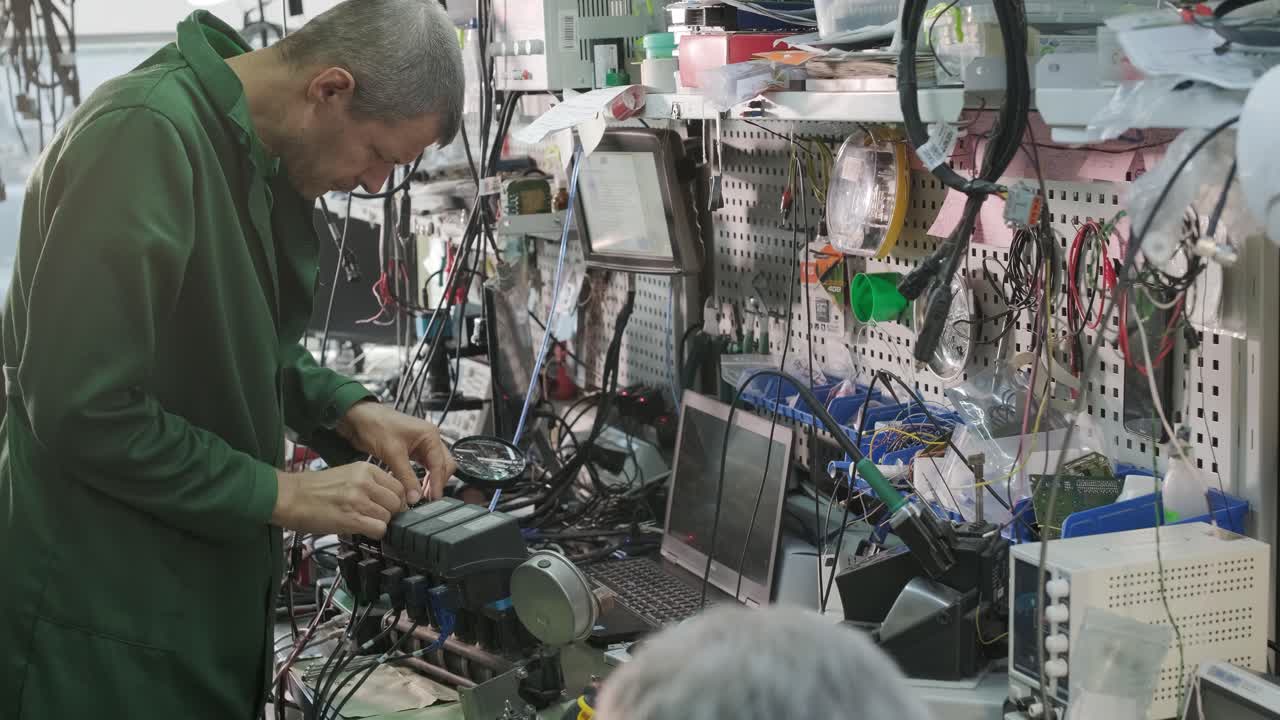전자 장비 수리 공장 - 엔지니어 기술자가 현미경 아래 전자 장치의 인쇄 회로 보드를 용접합니다.
