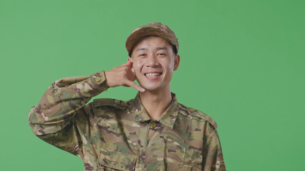 Close Up Of Asian Man Soldier Smiling And Making Call Me Gesture To Camera While Standing In The Green Screen Background Studio