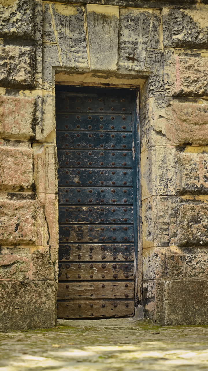 Antique wooden door with metal rivets in textured stone wall. Close up of a vintage weathered wood door set in an old coral limestone wall with historical architecture