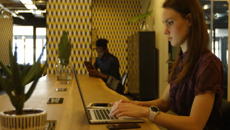 Side-view-of-young-caucasian-businesswoman-talking-on-mobile-phone-while-working-on-laptop-4k