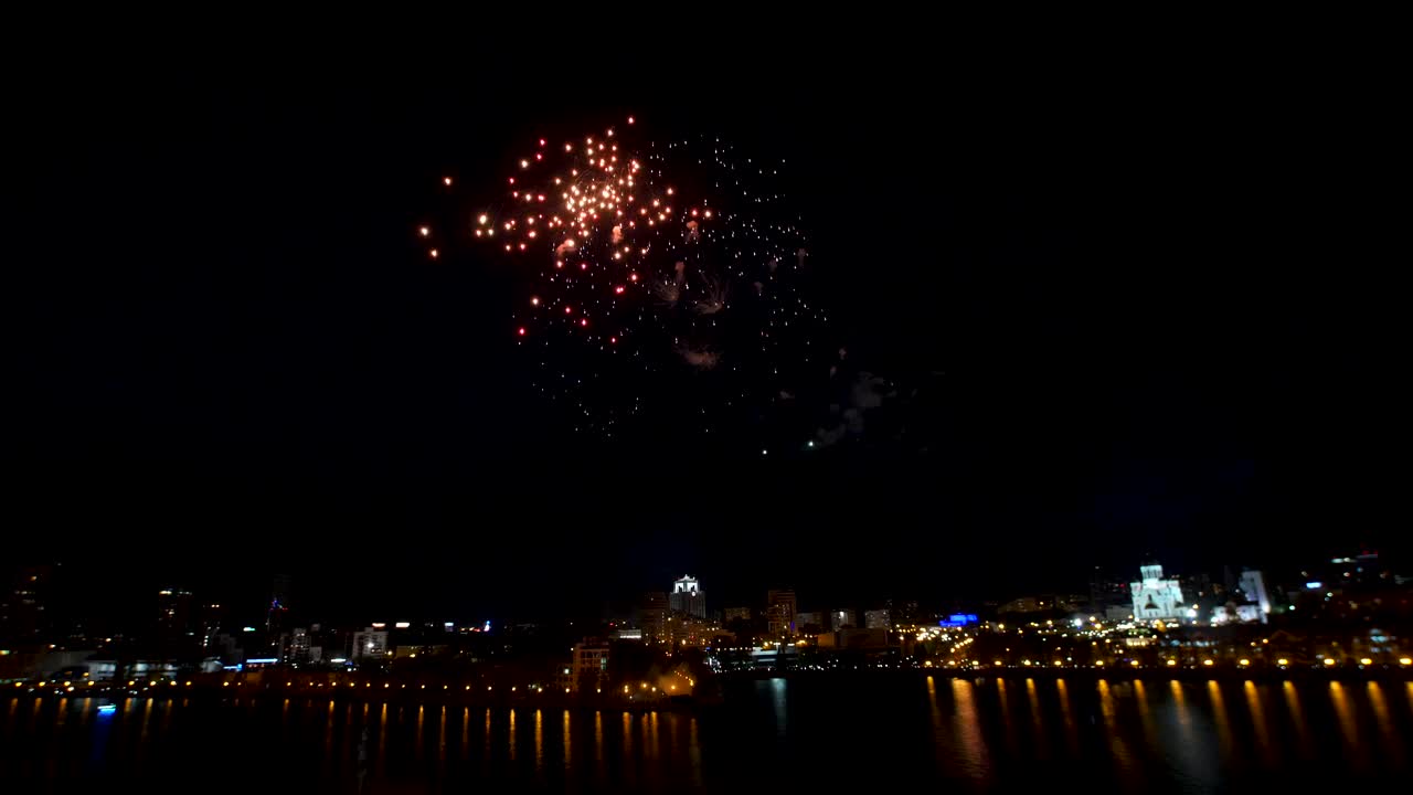 coloridos fuegos artificiales sobre una ciudad junto al río por la noche