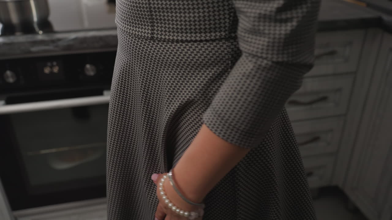 Close up of woman in patterned gown dancing in kitchen near stove and pot on counter, expressing joyful energy with graceful motion, creating warm home atmosphere in casual indoor setting