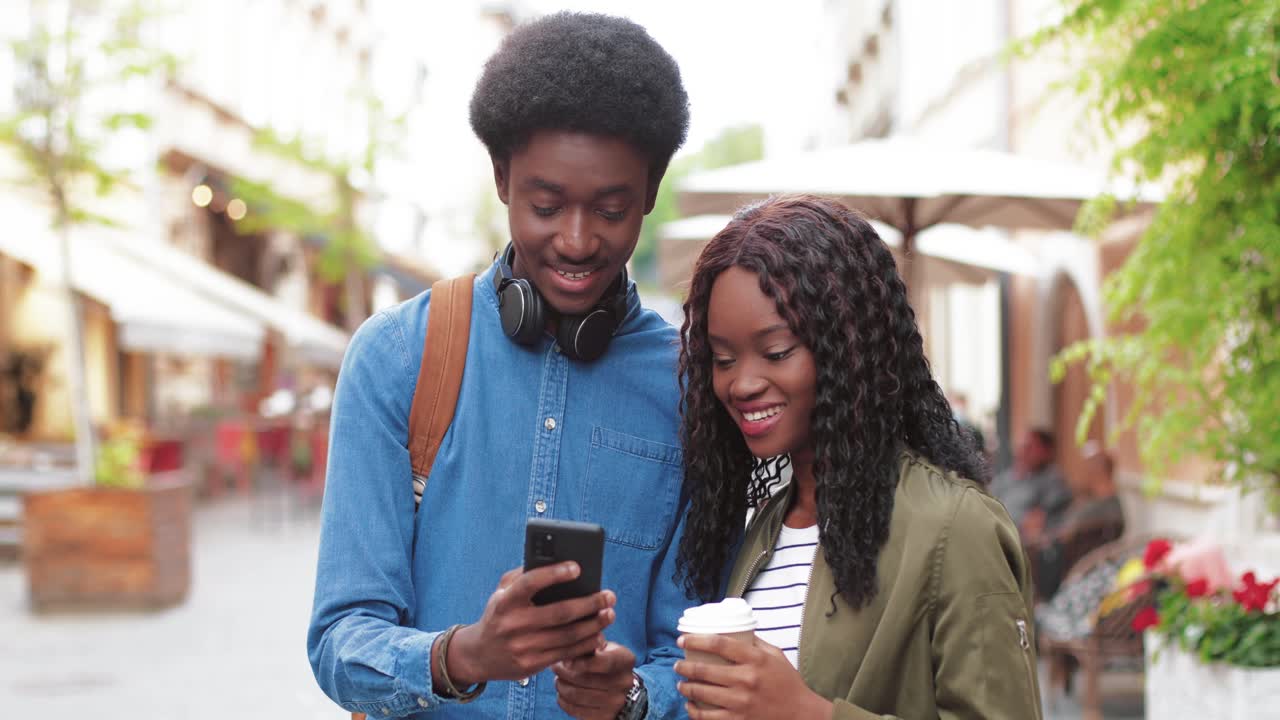 African american man and woman watching something in a smartphone in the street
