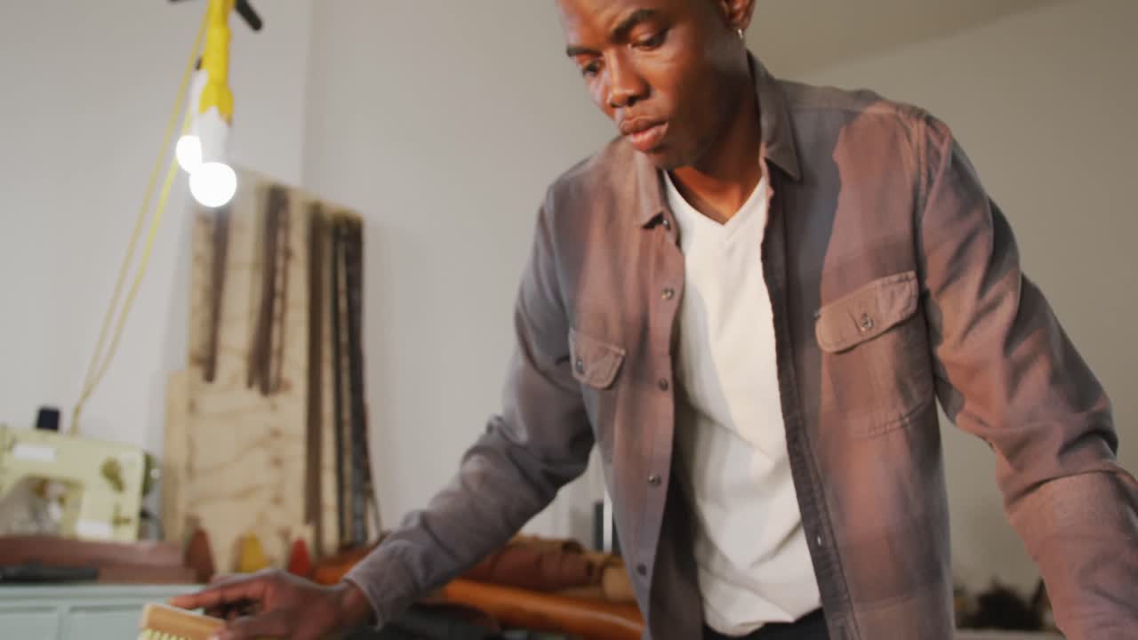 Focused african american craftsman brushing leather in leather workshop