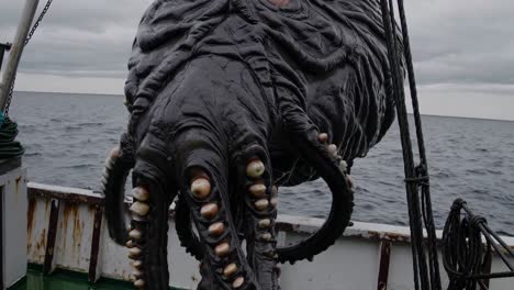 Massive fishing boat crew straining while hauling colossal, slimy black sea monster with menacing tentacles and sharp teeth from dark, mysterious ocean depths