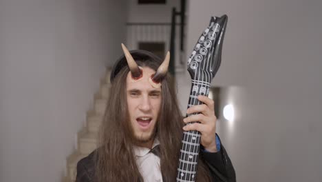 man in devil costume with inflatable guitar