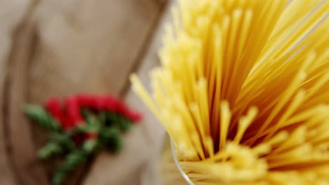 raw spaghetti arranged vertically in one glass jar on wooden background with colored pasta scattered