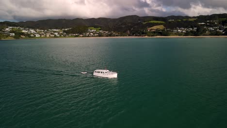 beautiful aerial tracking orbit shot of boat sailing, reveal of small beachfront settlement langs beach, new zealand