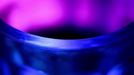edge of a glass with blue and purple lights of a pub, macro shot in close up view.