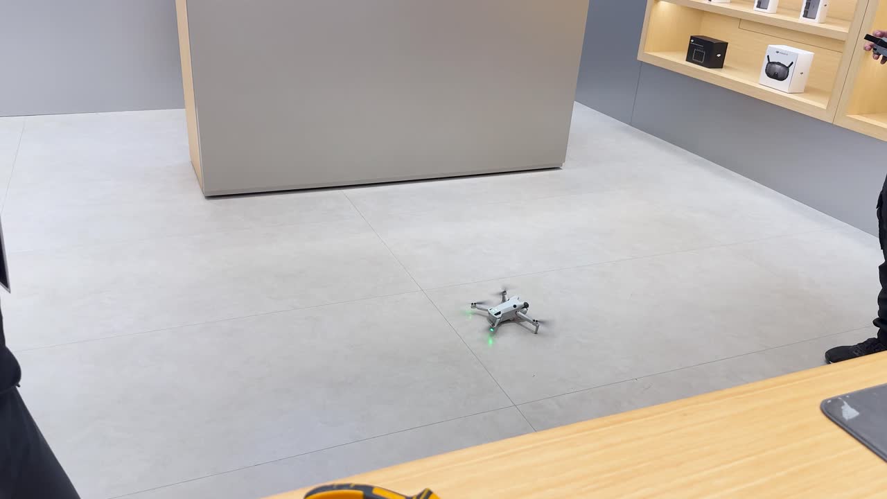 Two technicians examine and test a drone on the floor under bright, even indoor lighting