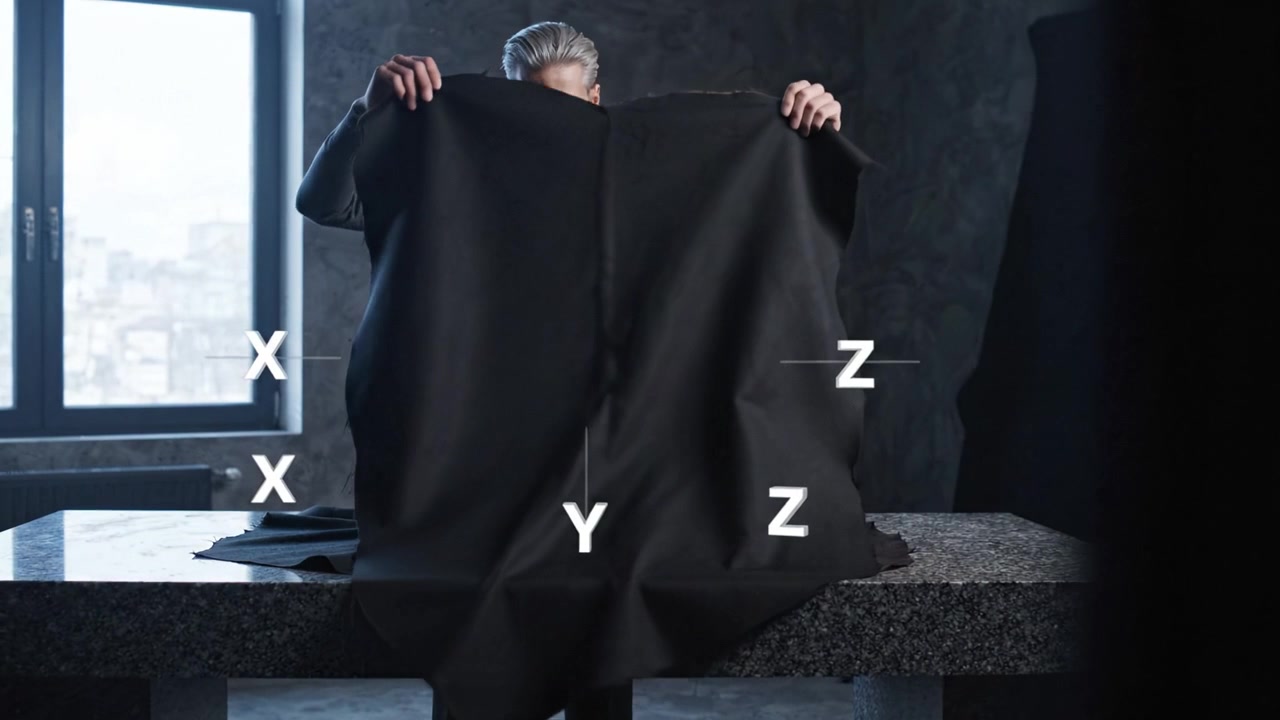Una persona concentrada vestida de gris organiza meticulosamente tela oscura sobre una mesa, iluminada por una luz suave en un elegante ambiente interior.