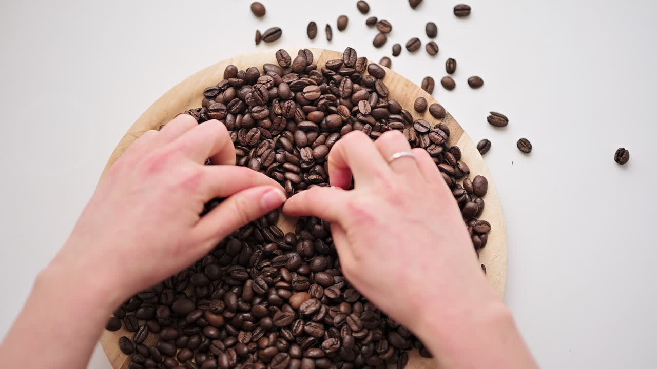 Hands touching and holding roasted coffee beans on a wooden tray