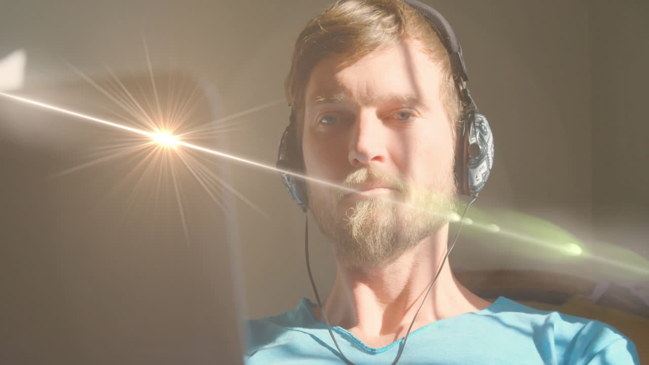 man wearing headphones focusing on laptop indoors, with animated tech data charts and lens flare