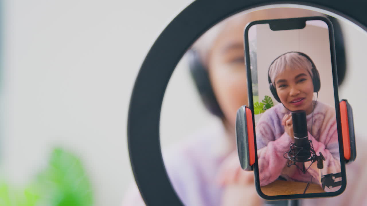 Kvindelig vlogger med hovedtelefoner og mikrofon livestreamer på mobiltelefonen