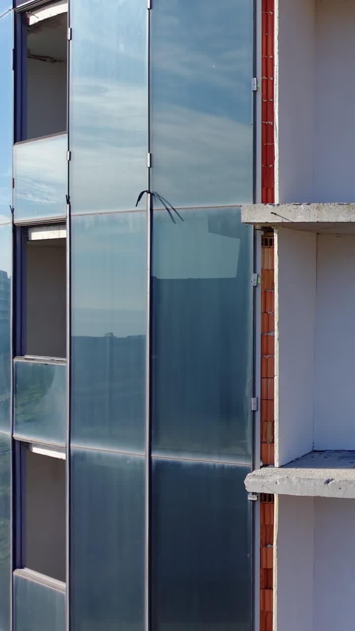 Detail of an unfinished facade showing glass panels, white insulation, and red ceramic bricks. Building with glass and bricks. Aerial view. Vertical video