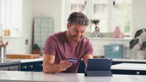 portrait of mature man with credit card using digital tablet at home to book holiday or shop