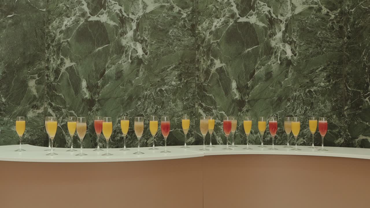 Fila de vibrantes bebidas naranjas y rojas en copas elegantes sobre una pared de mármol verde
