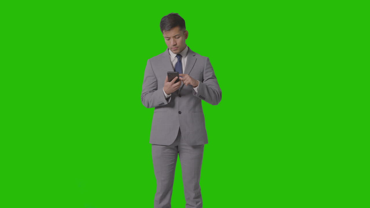 Three Quarter Length Studio Shot Of Businessman In Suit Looking At Mobile Phone Against Green Screen 4