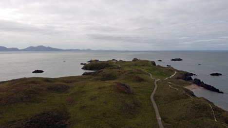 Aerial-rising-view-Ynys-Llanddwyn-island-Anglesey-coastal-walking-trail-with-Snowdonia-mountains-across-the-Irish-sea