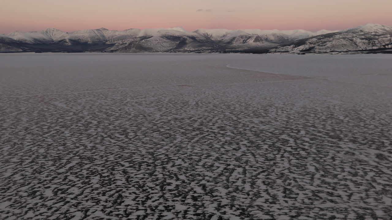 Frozen Kluane Lake At Sunset In Destruction Bay, Yukon Territory, Canada. aerial tilt-up shot