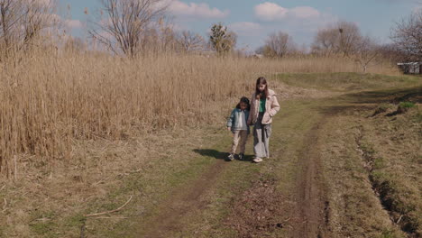 two girls walking hand-in-hand on a dirt path through a field