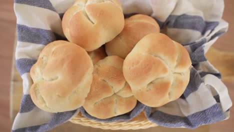 freshly baked kaiser rolls in woven basket on wooden background, top down view