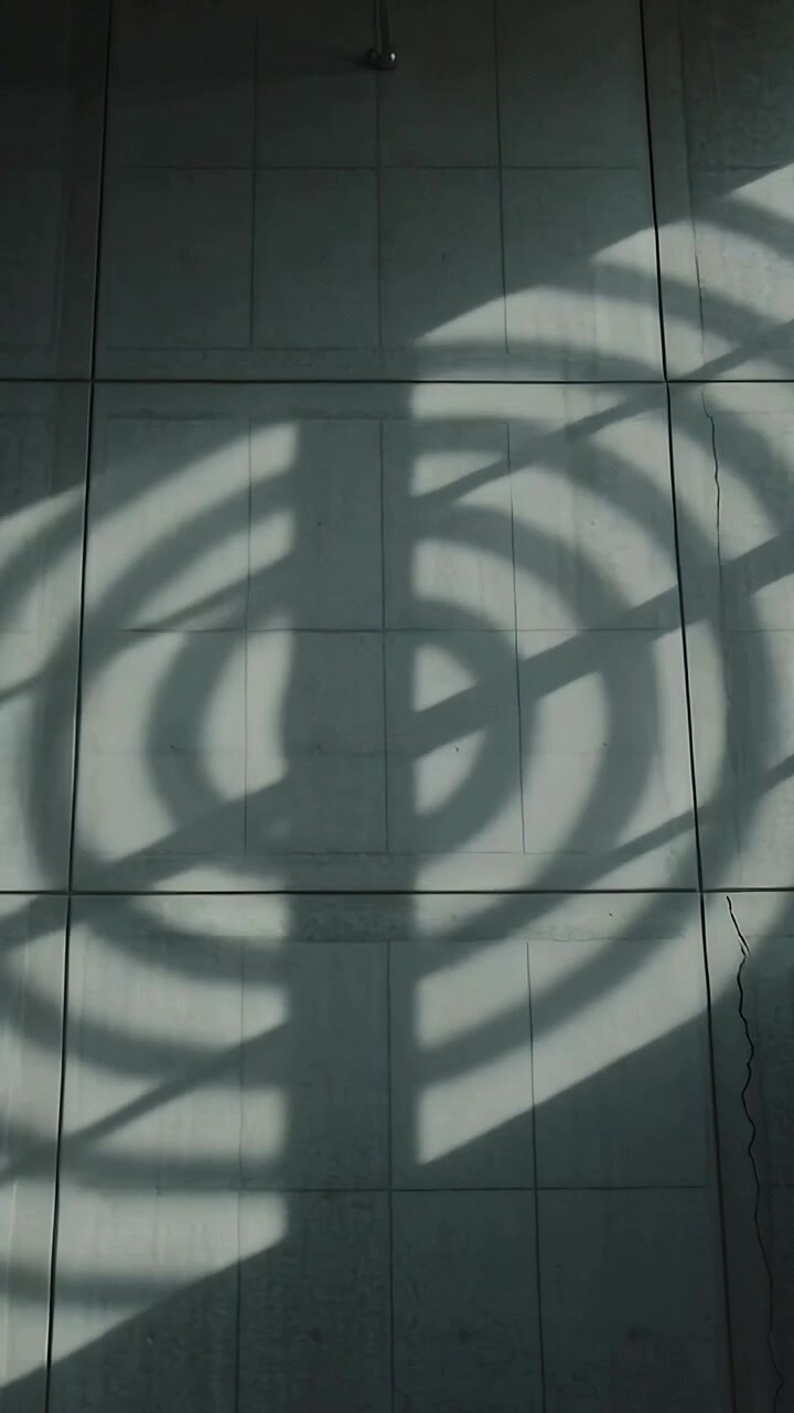 Vertical video: Sliding grille shadow pattern moving right across lobby tiled wall via sunlight