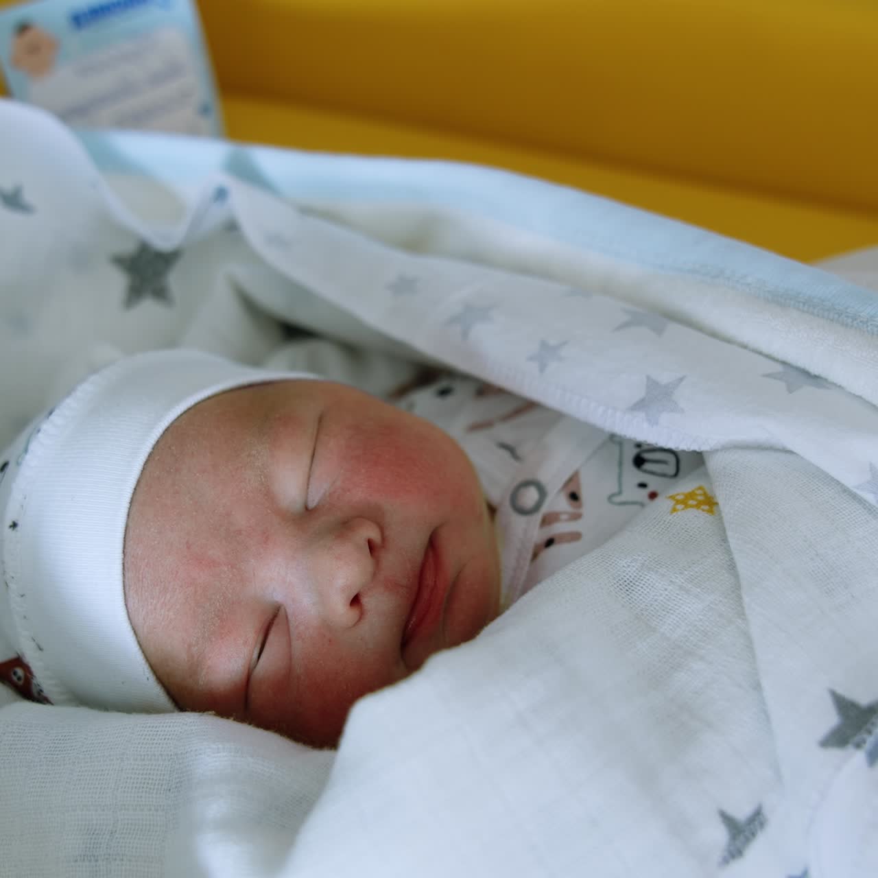 Neonato di pochi giorni con cappellino, maglietta e copertine. Bambino adorabile che apre la bocca nel sonno. Primo piano