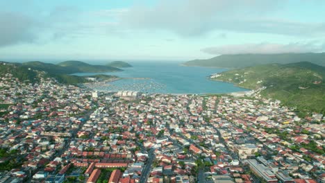 Panorama-Drohnenansicht-Des-Strandes-Von-Dos-Anjos,-Arraial-Do-Cabo,-Brasilien,-Tropische-Landschaft,-Grüne-Hügel,-Küstenviertel-Und-Blau-Bewölkte-Skyline