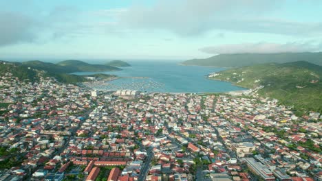 vista panorámica de drones de la playa de dos anjos arraial do cabo brasil paisaje tropical, colinas verdes, barrio costero y horizonte nublado azul