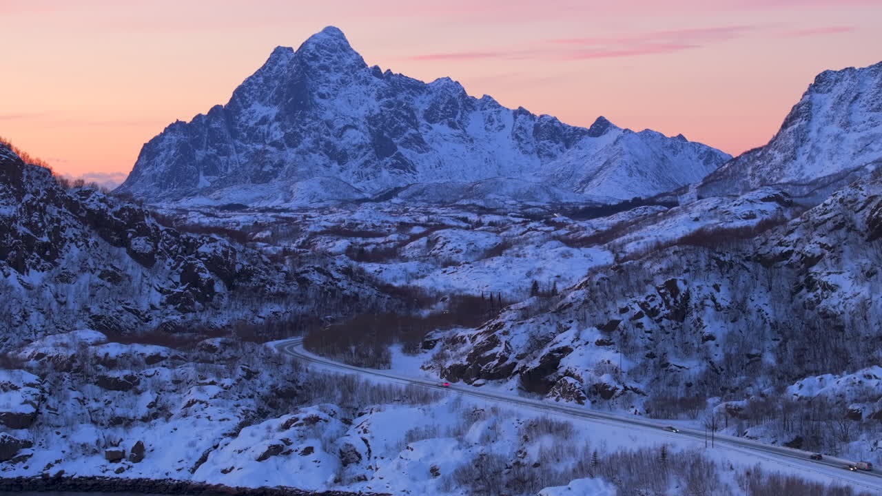 Cars driving on highway through snowy landscape, majestic mountain peak towering in background, Lofoten, Norway, aerial view