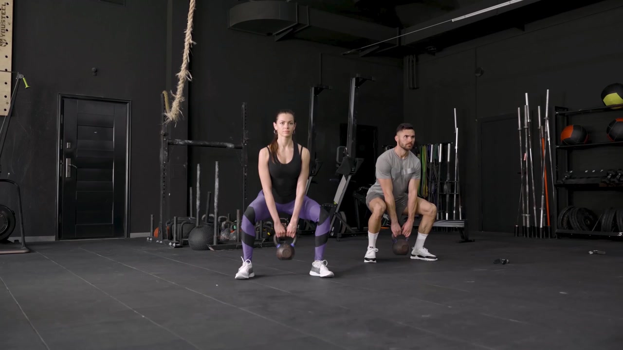 Uomo e donna che eseguono squat con kettlebell in una palestra moderna