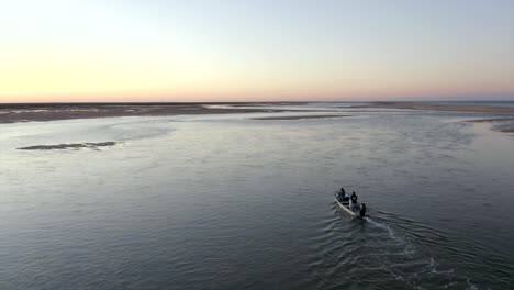 small boat with two people in it going out to sea between lovely beaches during sunset in praia, portugal